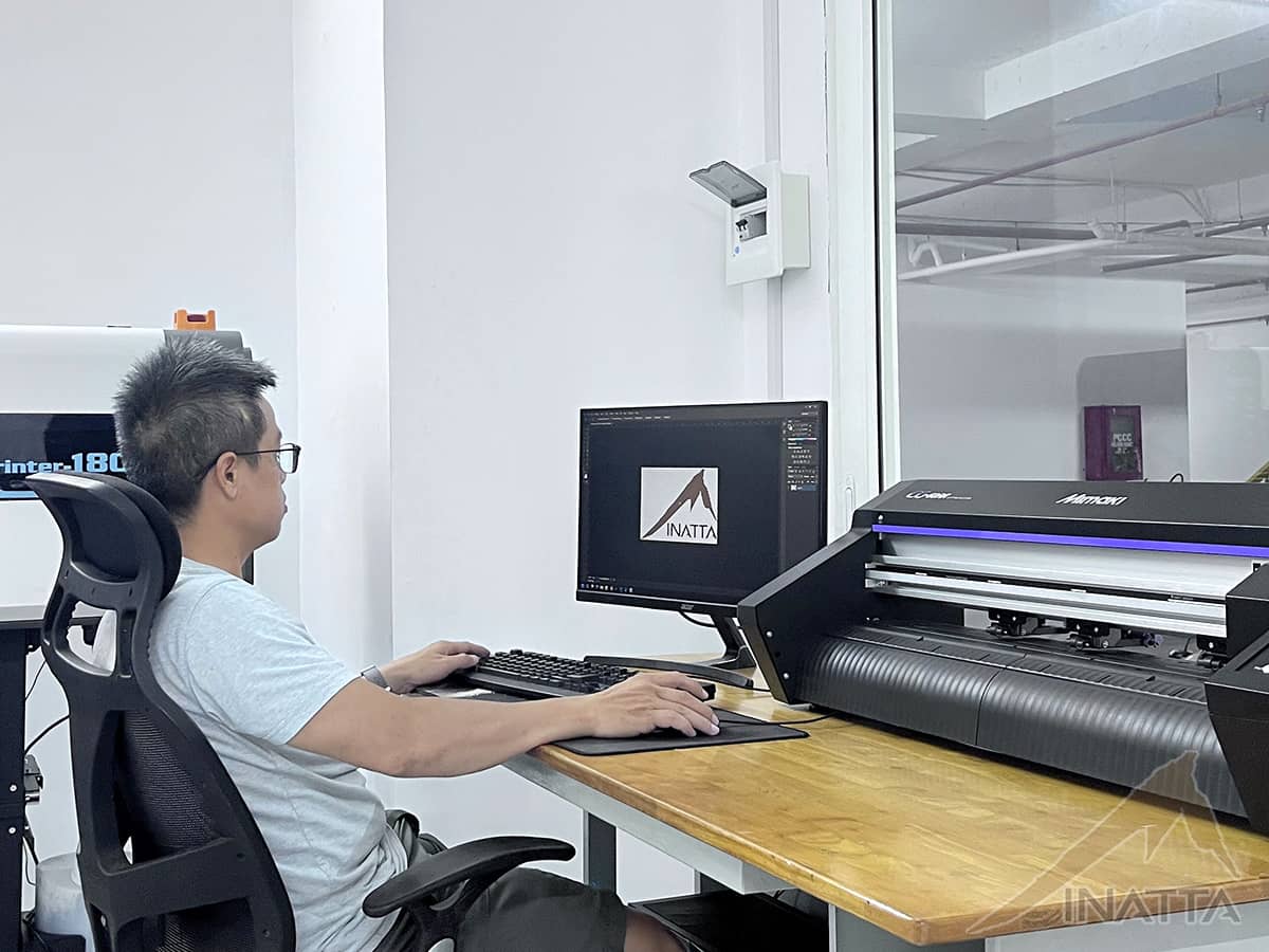 Nhân viên thiết kế INATTA dàn file trên máy tính, máy bế decal Mimaki đặt ngay cạnh bàn làm việc