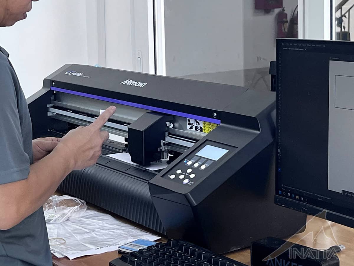 Nhân viên kiểm tra vị trí dao và vật liệu trên máy bế Mimaki trước khi cắt tem sticker